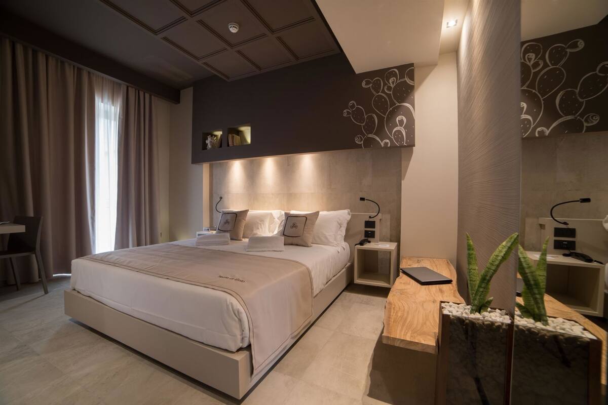 A modern hotel room with a large bed, bedside tables, a desk, and a decorative plant.