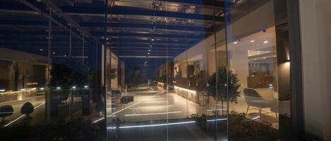 A modern hotel interior with a glass facade, a reception area, and a seating area with plants.