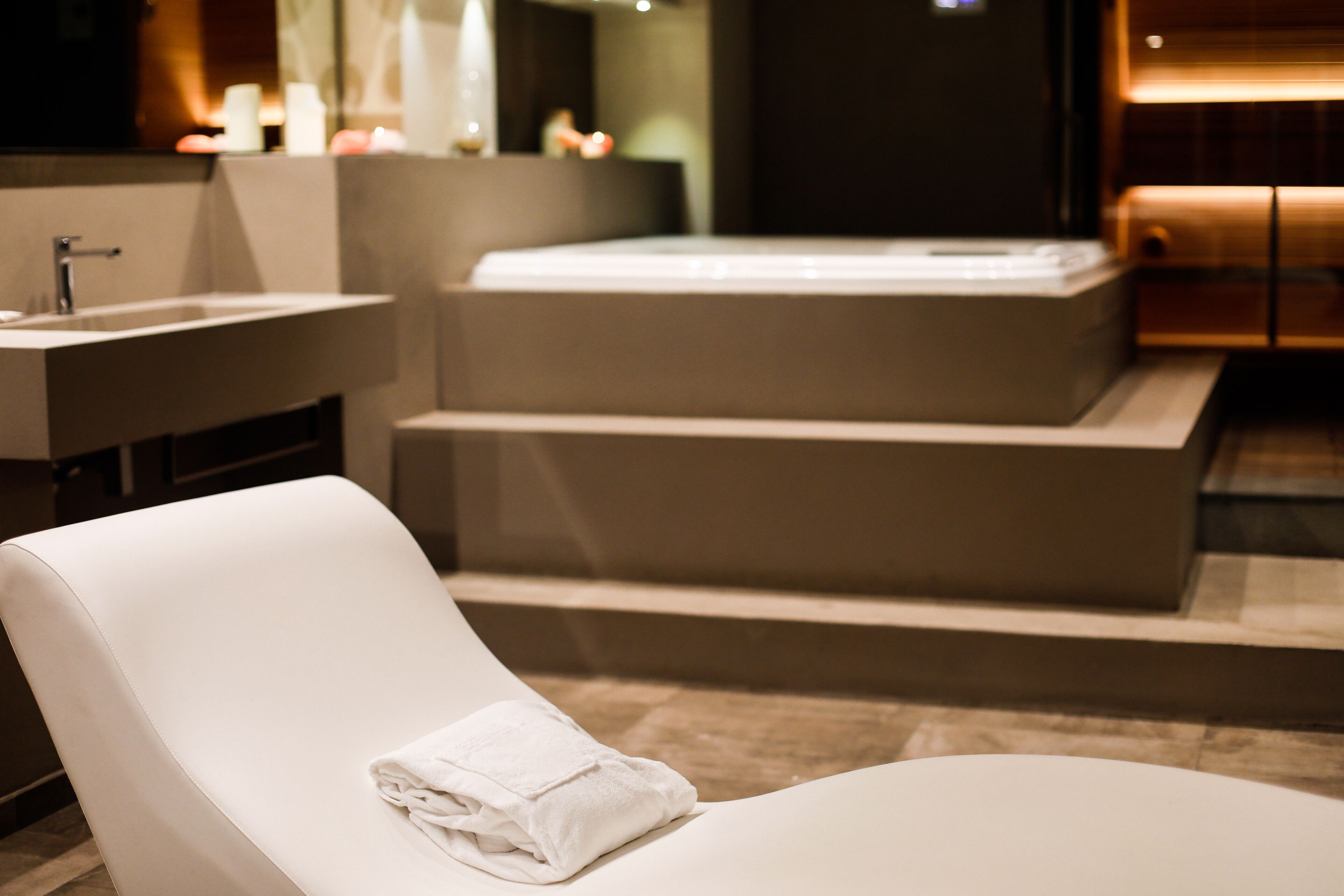 A modern bathroom with a large bathtub, a sink, and a towel on a chair.