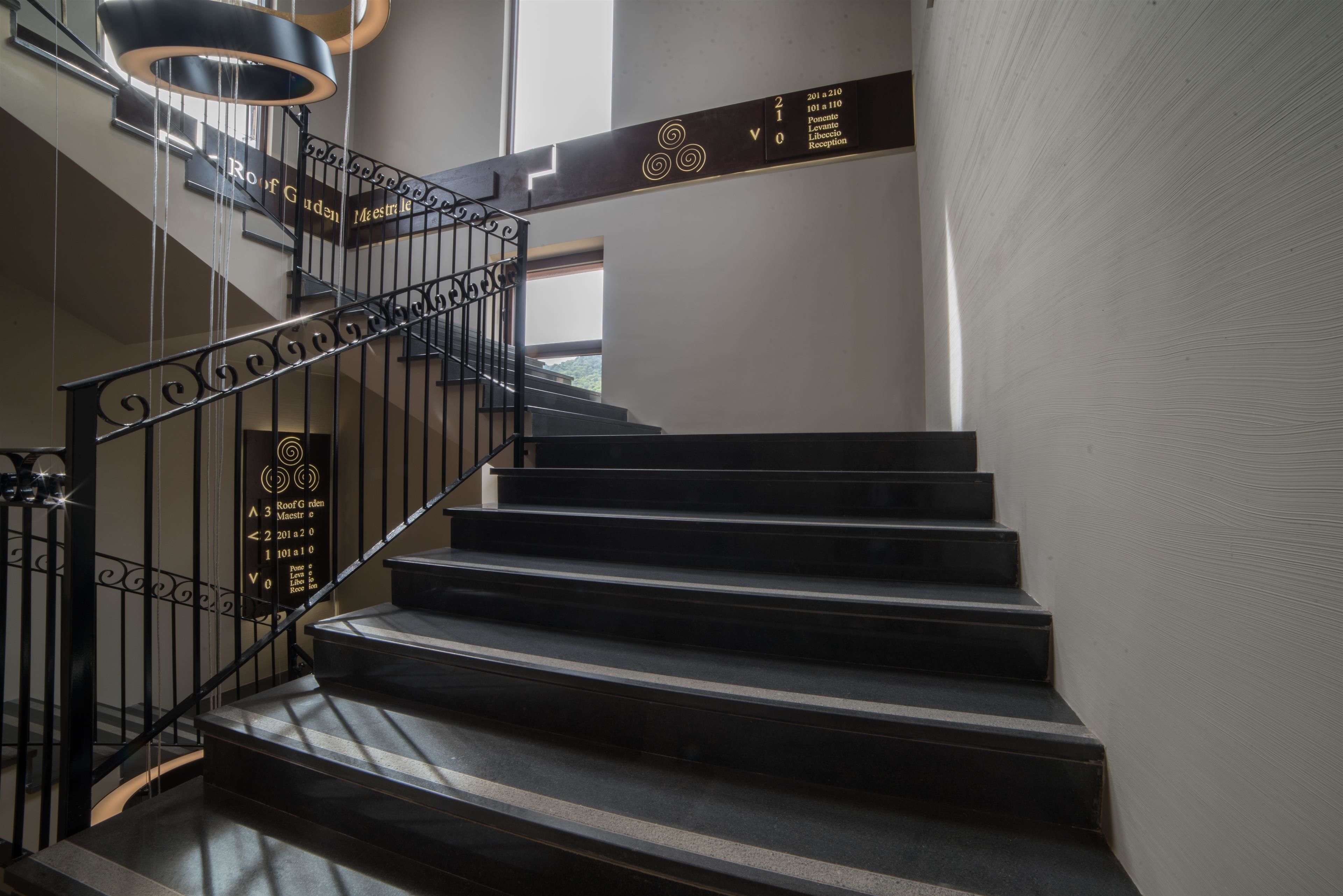Escadaria moderna com corrimãos pretos e uma placa indicando direções para diferentes andares.