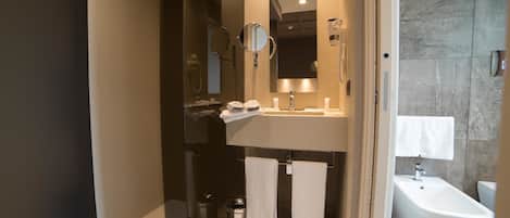 A modern bathroom with a glass-enclosed shower, a sink with a mirror, and a bidet.