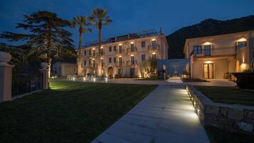 A multi-story hotel with a well-lit exterior, a paved walkway, and a landscaped lawn.