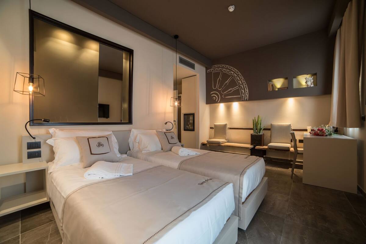 A hotel room with two beds, a desk, a chair, a large mirror, and a decorative wall piece.