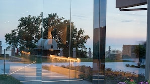 Een modern gebouw met een glazen gevel die het omliggende landschap weerspiegelt, inclusief bomen en een waterpartij.