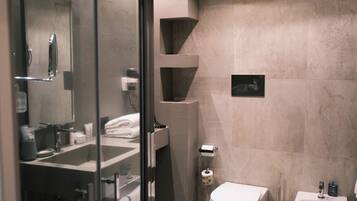 A modern bathroom with a glass shower enclosure, a toilet, bidet, and a sink.