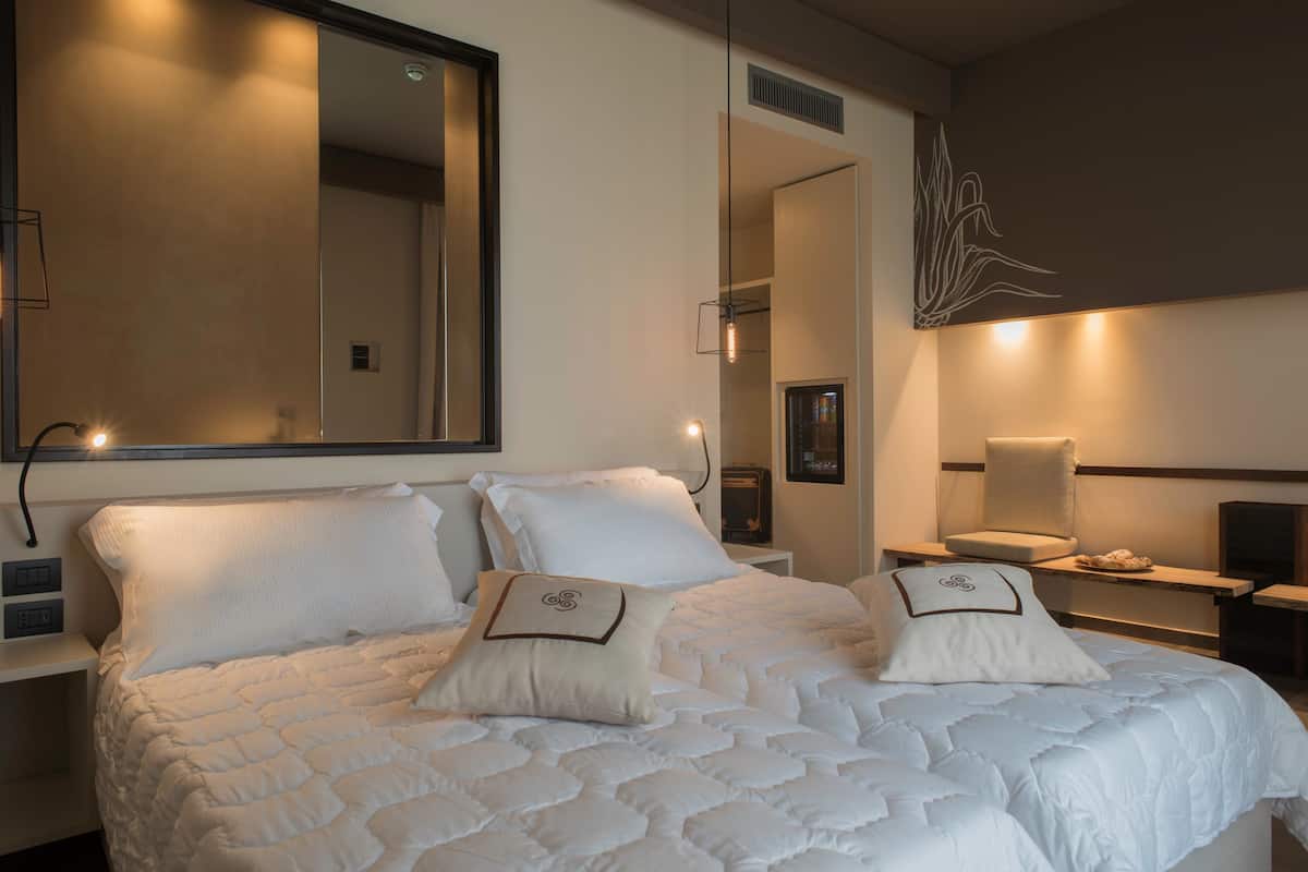 A hotel room with a large bed, a bedside table, a chair, and a mirror on the wall.