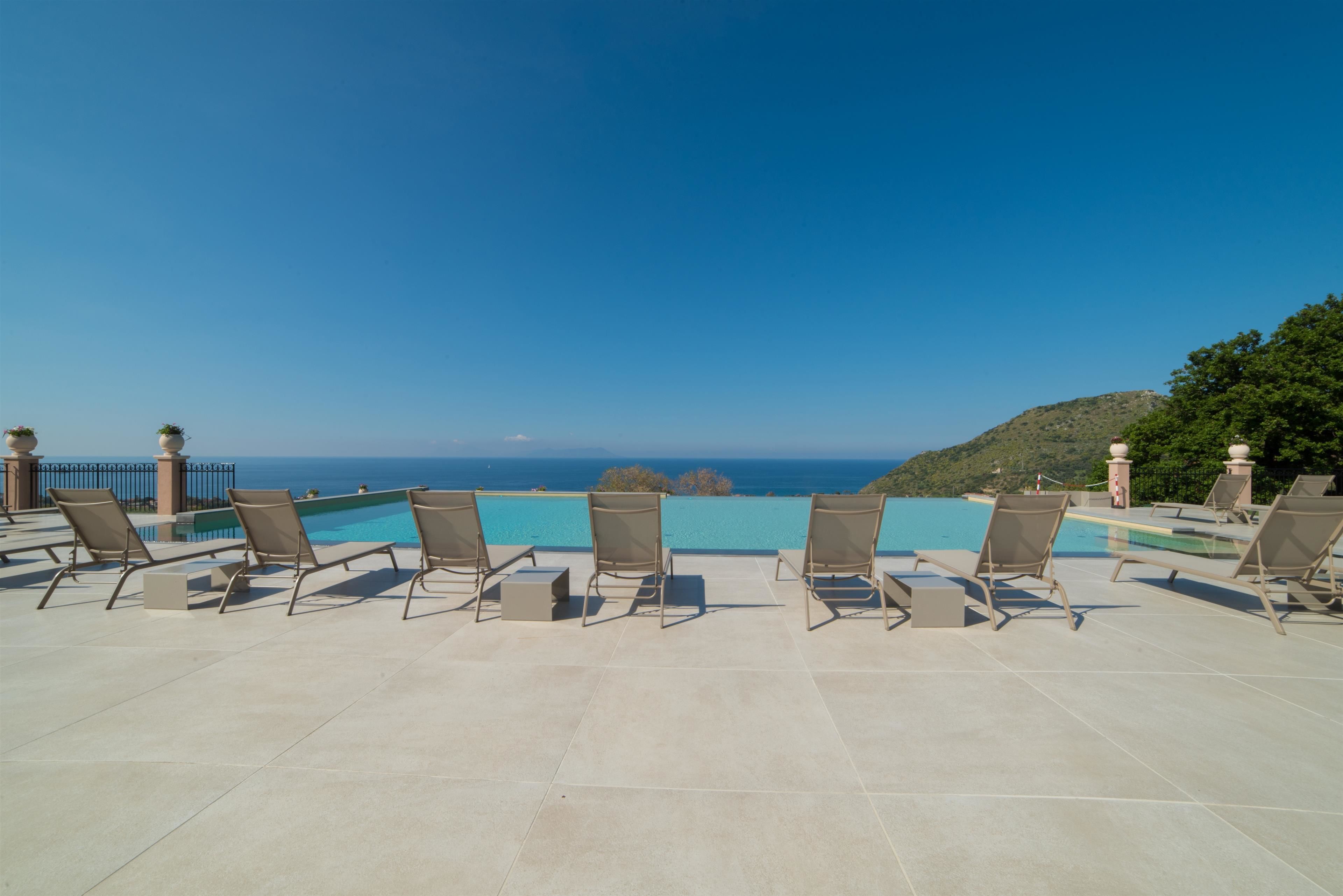 A poolside area with lounge chairs and a view of the ocean.