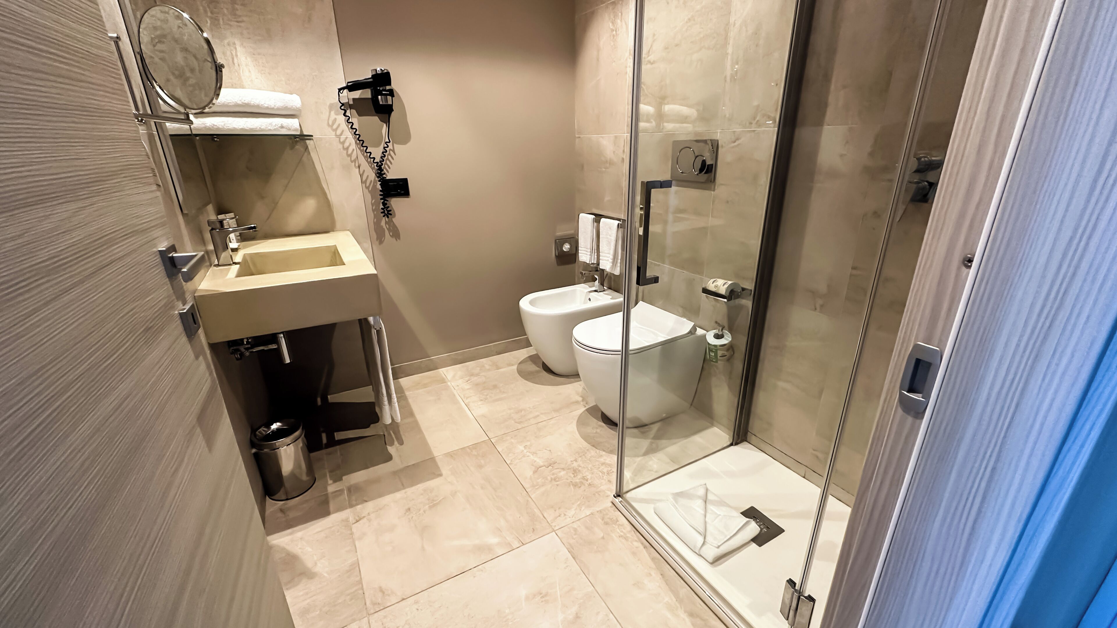 Et moderne badeværelse med brusekabine i glas, toilet og håndvask med spejl over.