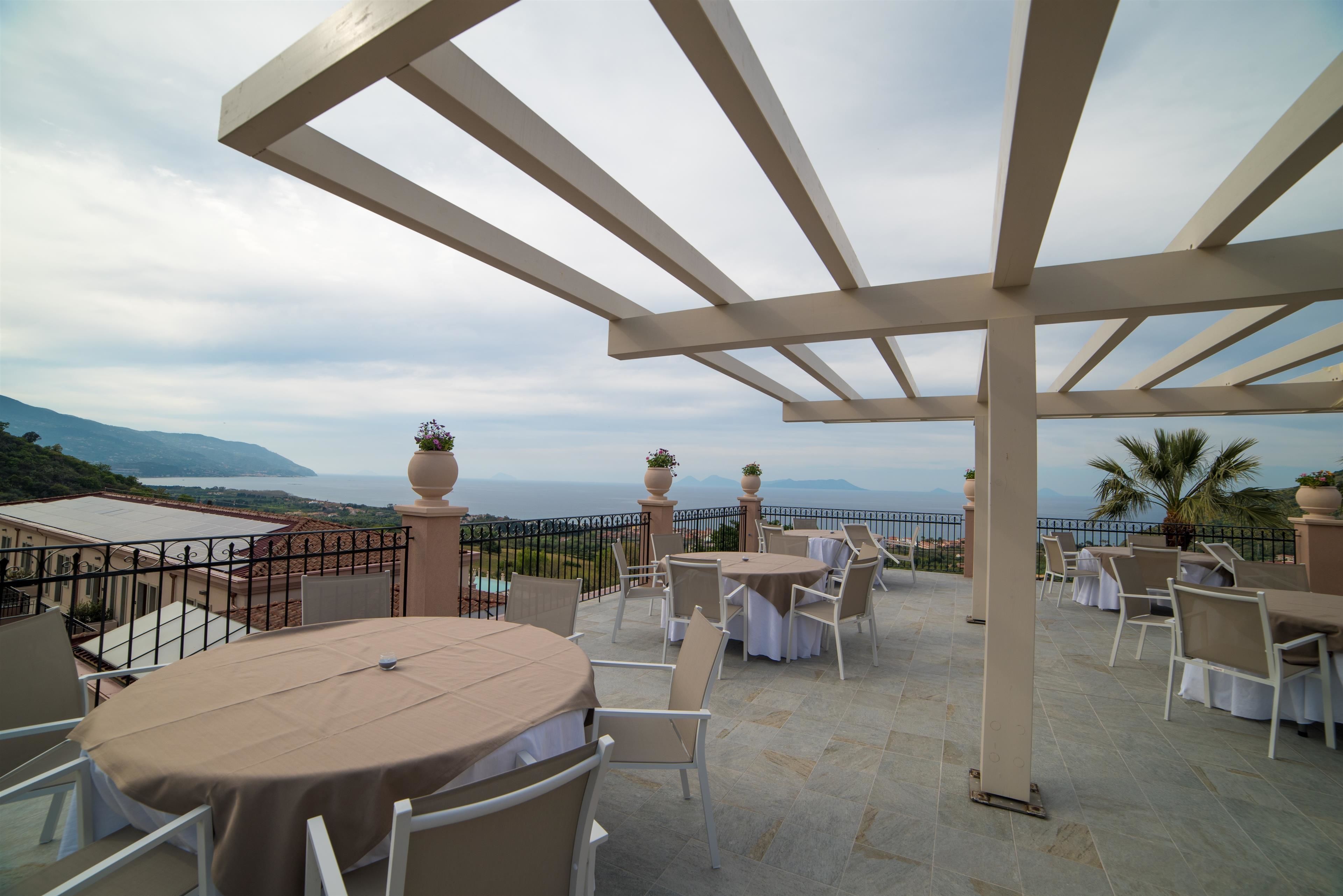 A terrace with tables and chairs, overlooking a scenic view of the sea and mountains.