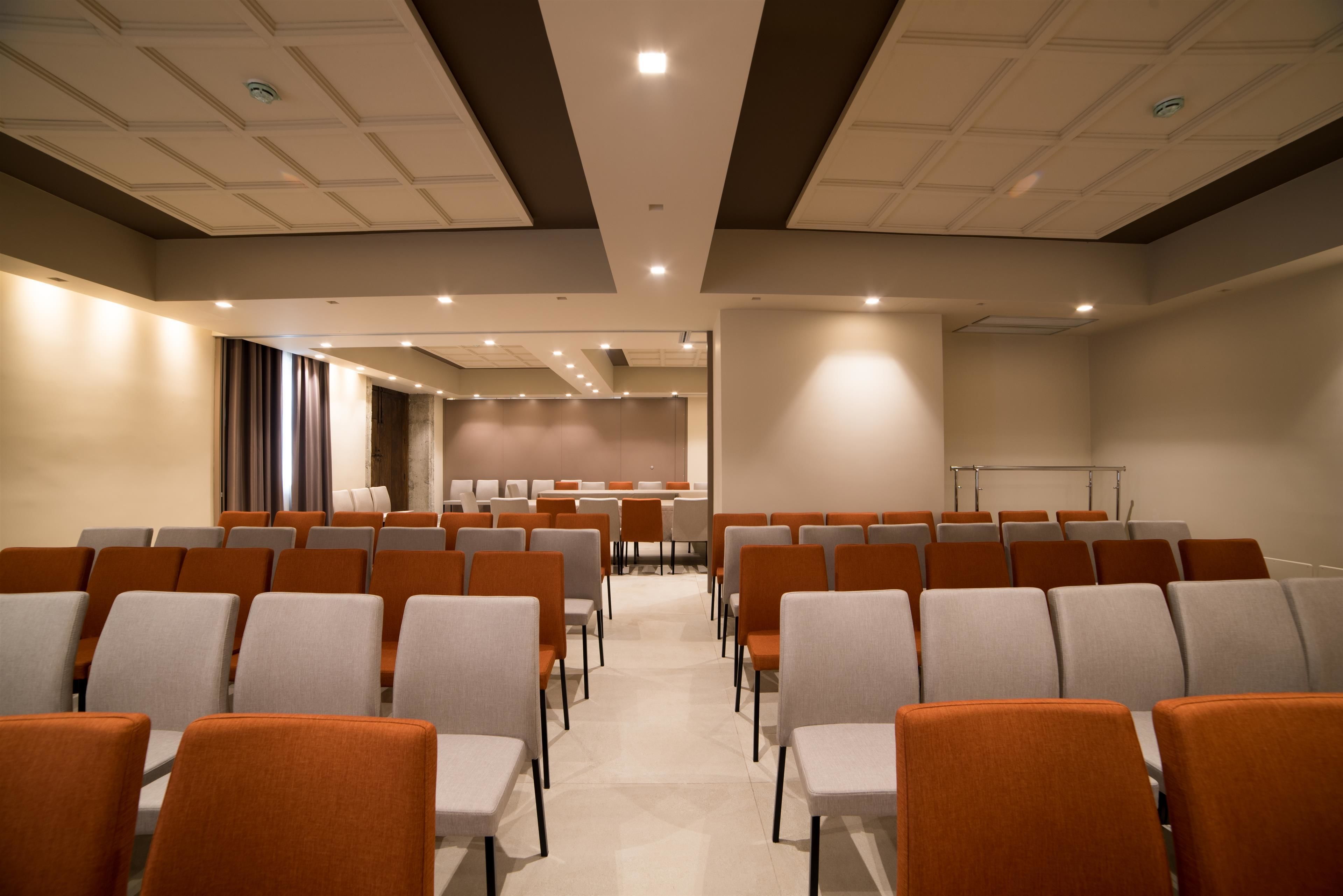 Une salle de conférence avec des rangées de chaises, une scène et un écran de projection.