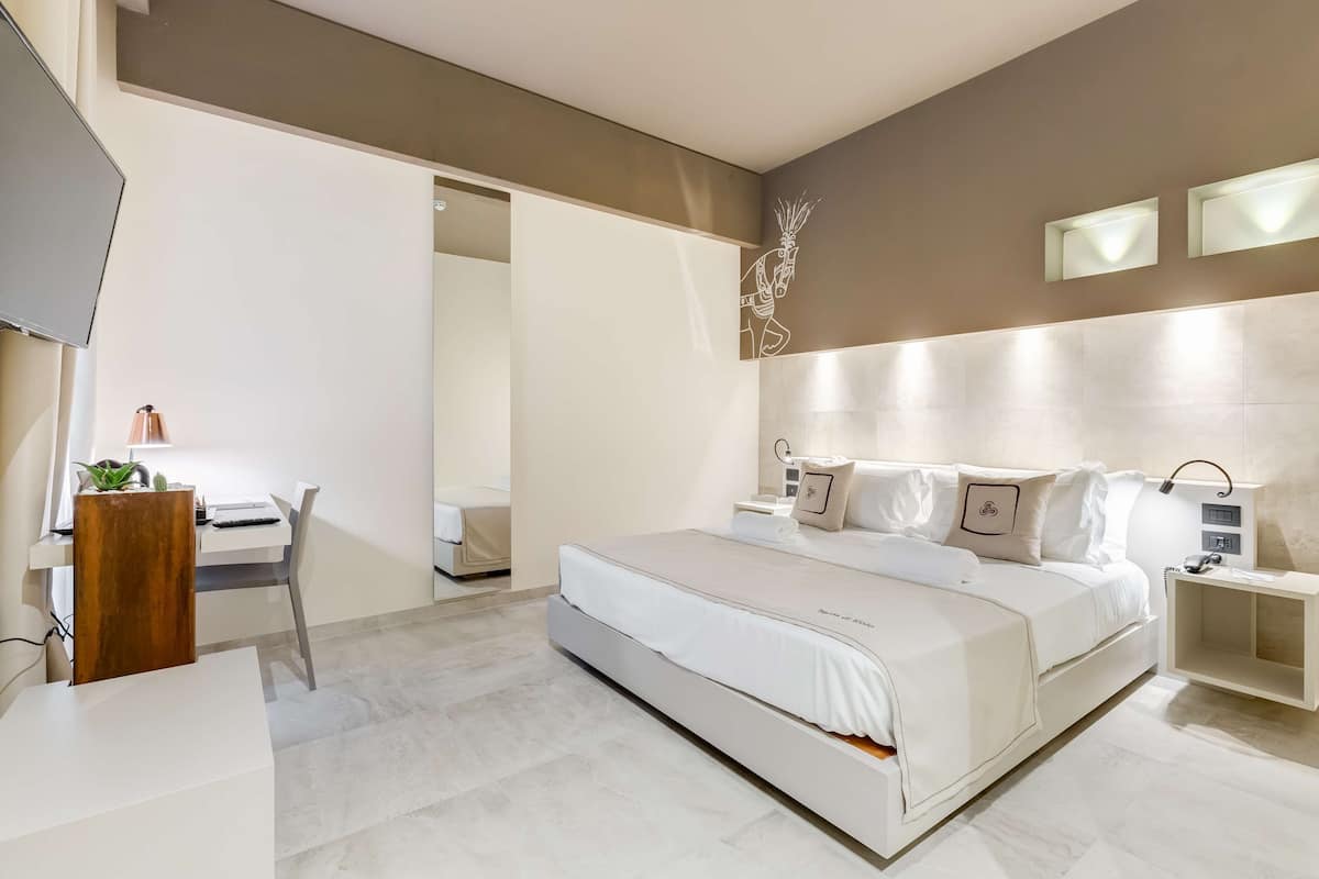 A modern bedroom with a large bed, a desk with a computer, and a TV.