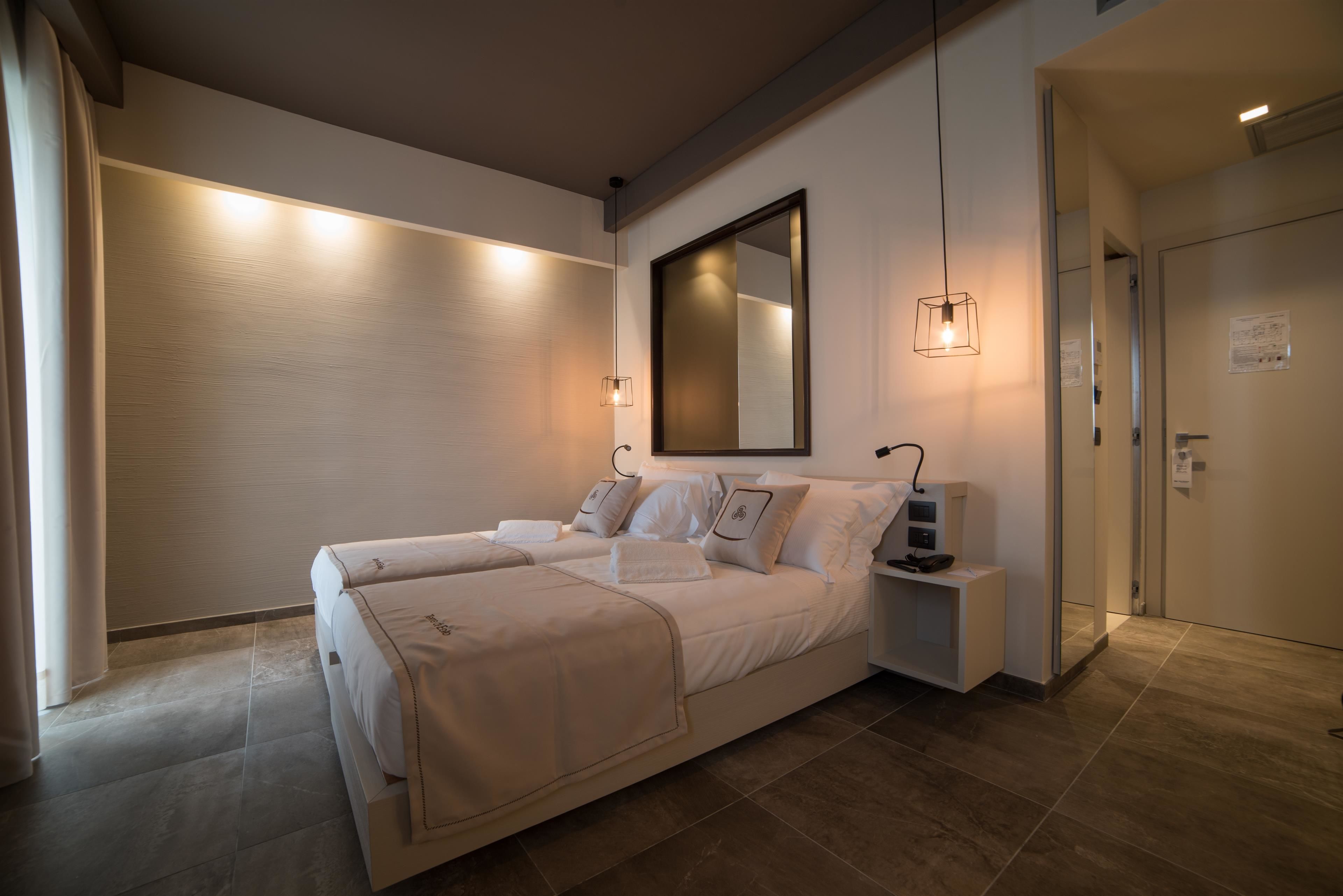 A modern hotel room with a large bed, bedside tables, a mirror, and a nightstand.