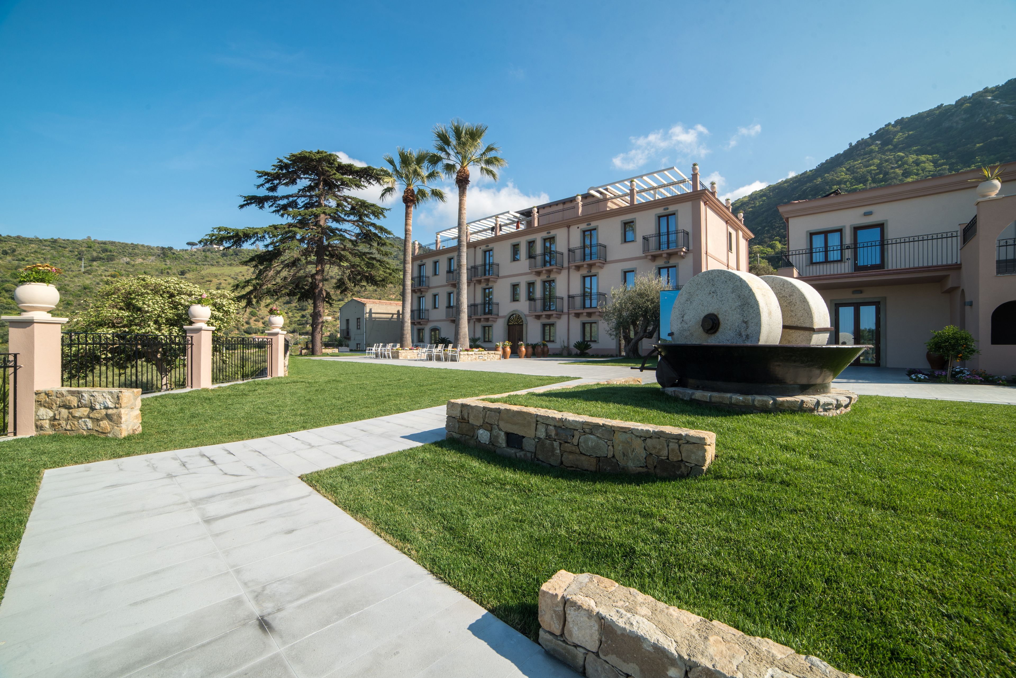 Un patio de hotel con una fuente central, muros de piedra y un sendero adoquinado.