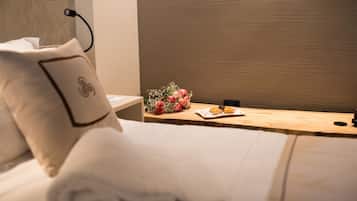 A neatly made bed with a pillow, a wooden bedside table with a bouquet of flowers and a plate of cookies, and a wall with a textured pattern.