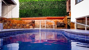 A swimming pool with a stone wall and a metal ladder.