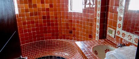 A bathroom with a red-tiled jacuzzi, a white sink, and a mirror with floral tiles.
