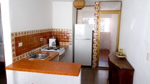 Cocina compacta con estufa a gas, pileta y refrigerador blanco.