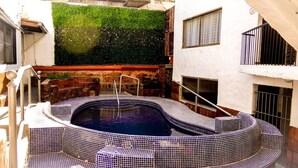 A hot tub with a tiled edge, a green wall with flowers, and a balcony with a railing.