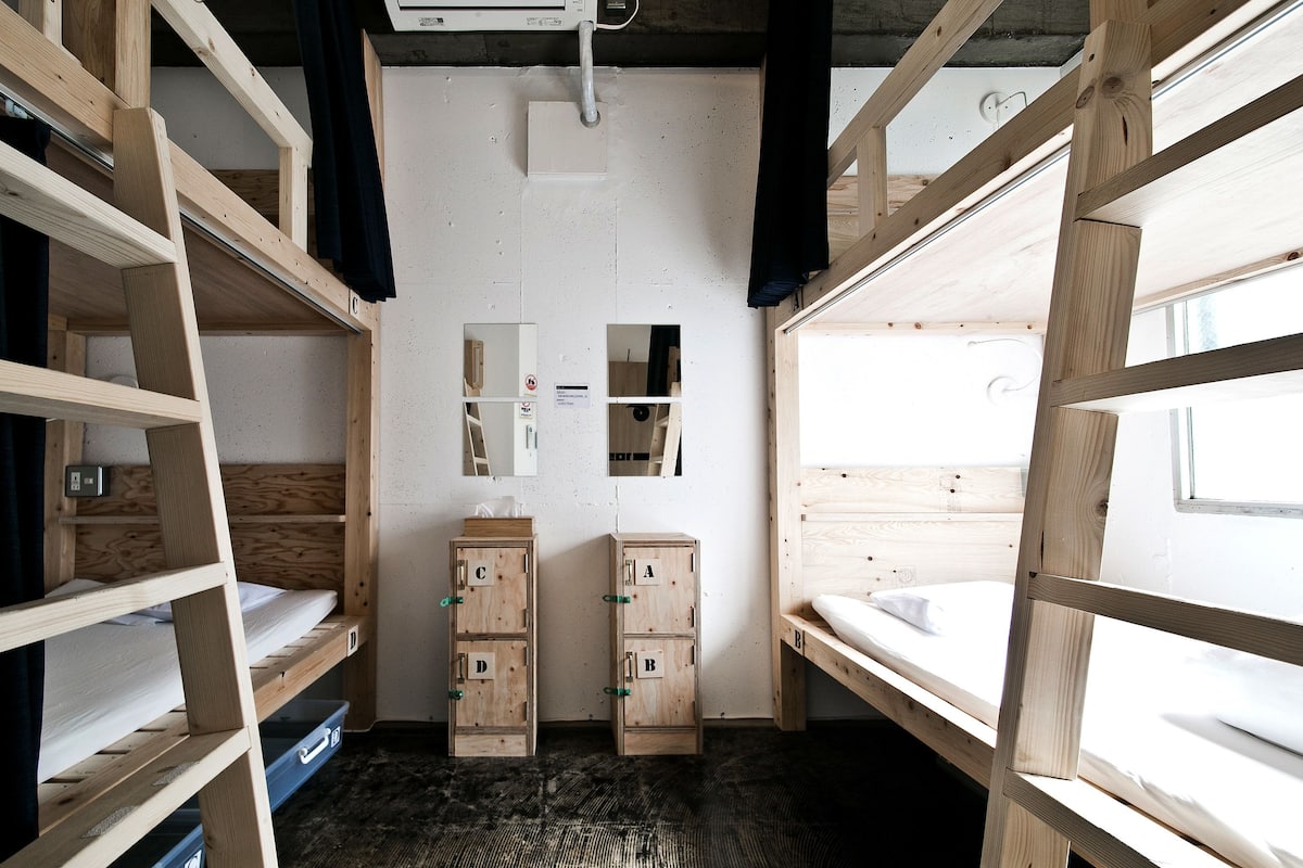 A dormitory room with bunk beds, a small storage unit, and a window.