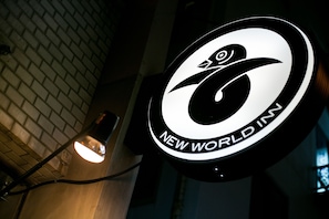 A circular sign with a bird logo and the text "NEW WORLD IN" against a brick wall background. - NEW WORLD INN - Hostel (Osaka)