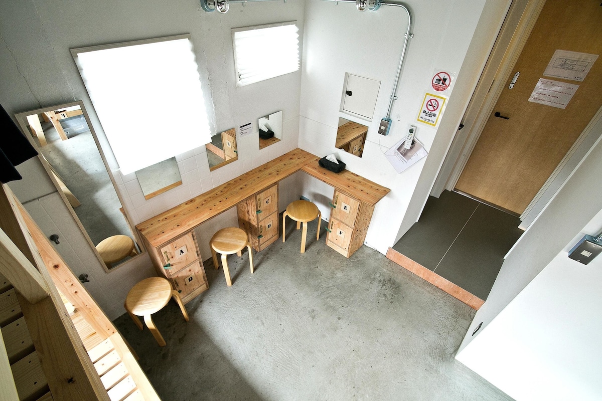 A small, compact bathroom with a wooden vanity, three stools, and a mirror.