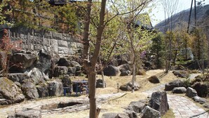 A stone pathway surrounded by large rocks and trees, leading to a traditional building with a tiled roof. - Oyado Nozawa (Takayama)