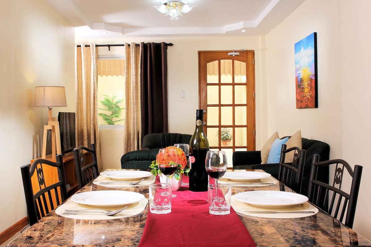 Comedor con una mesa dispuesta para seis personas, una botella de vino y un florero con flores.
