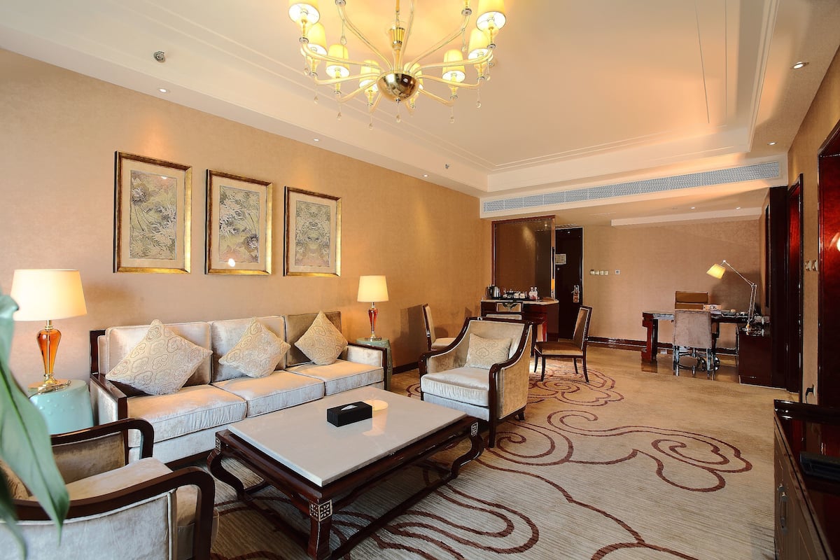 Un vestíbulo de hotel con un sofá, sillones, una mesa de centro, una araña y obras de arte enmarcadas en la pared.