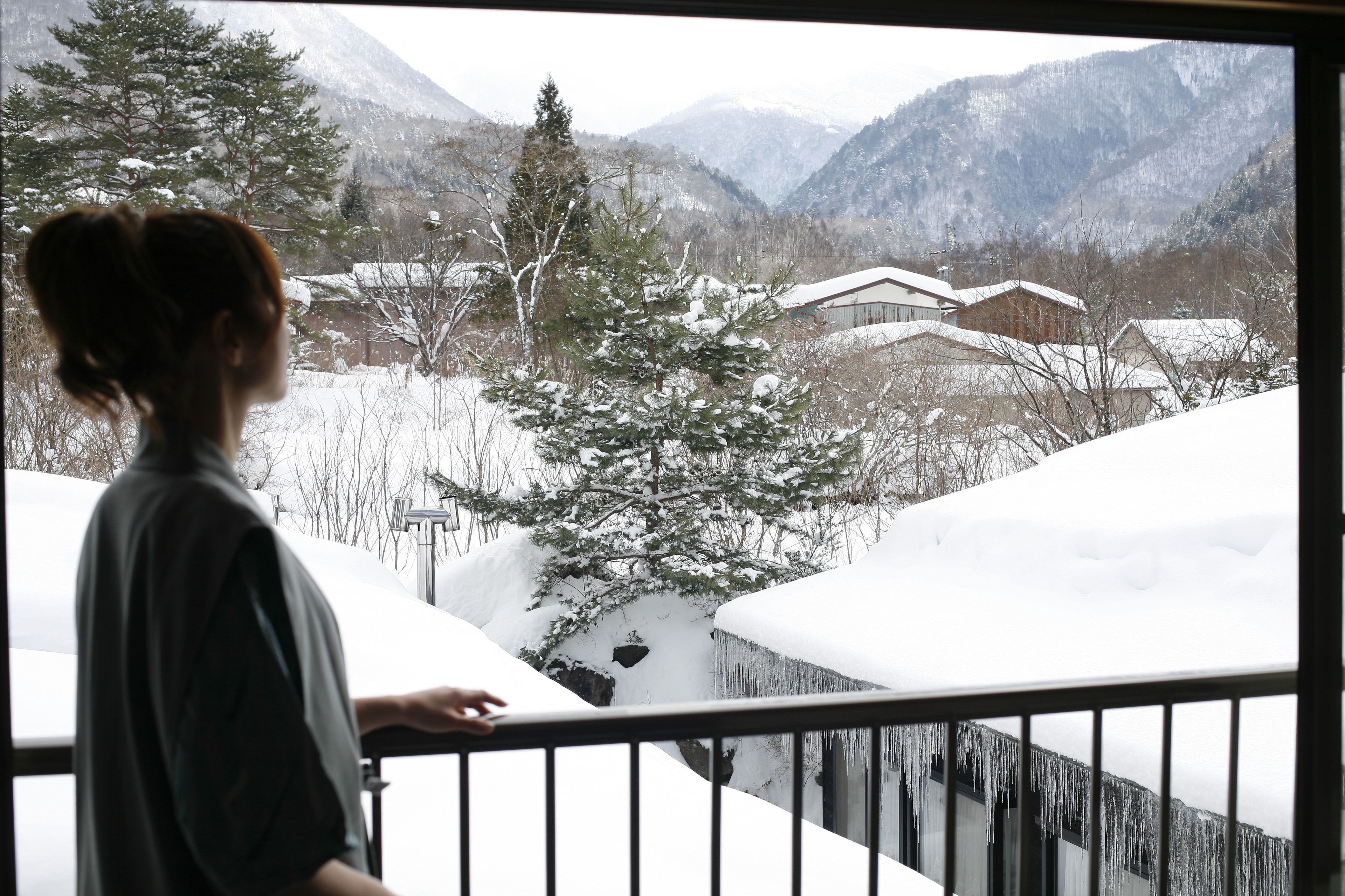 A person standing by a window overlooking a snowy landscape with mountains in the background.