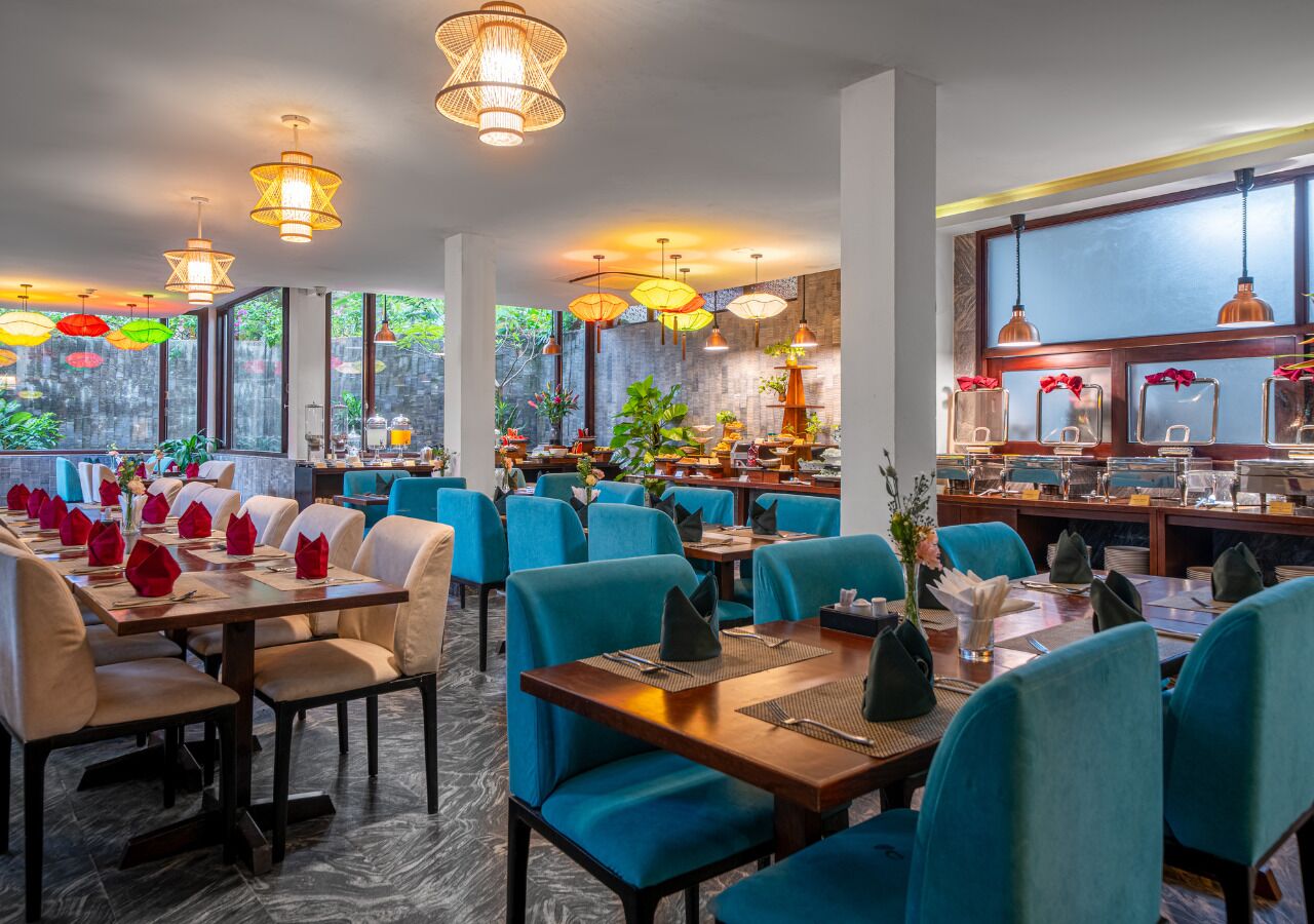 A restaurant with multiple tables and chairs, large windows, and hanging pendant lights.