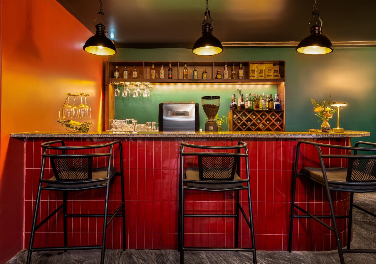 Eine Bar mit roten Fliesenwänden, schwarzen Barhocker und Deckenleuchten.