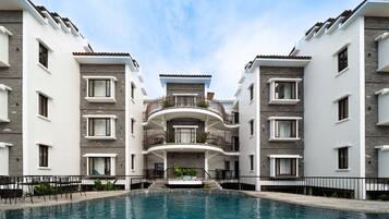 A modern hotel with a central pool, balconies, and a clear sky.