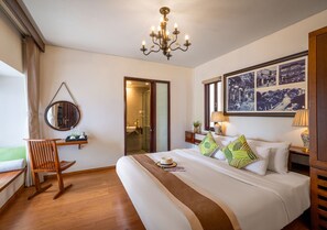 A hotel room with a large bed, a wooden rocking chair, a chandelier, and a framed picture on the wall. - Faifo Boutique Hotel & Spa (Da Nang)