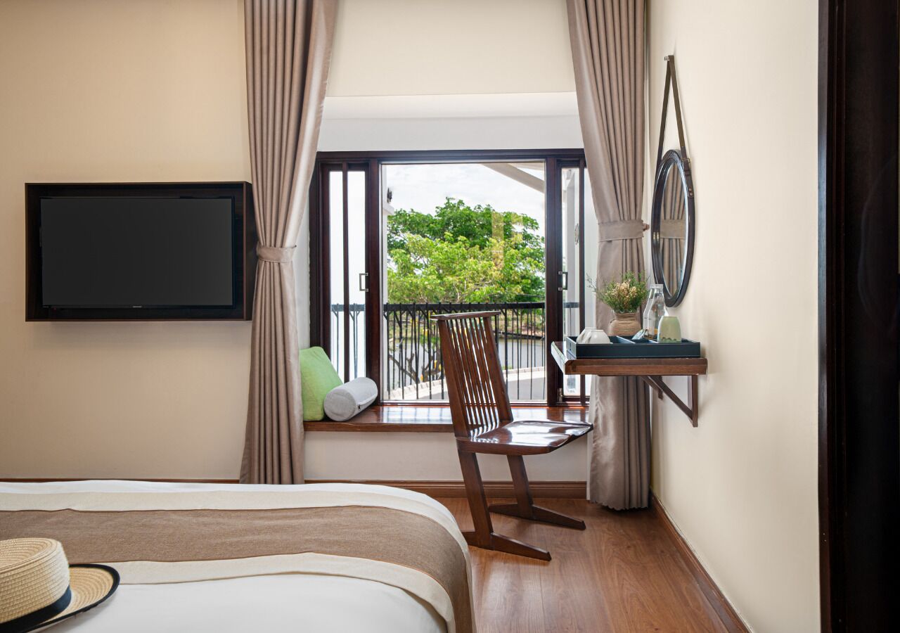 A hotel room with a bed, a chair, a TV, a window with a view, and a small table with a plant.