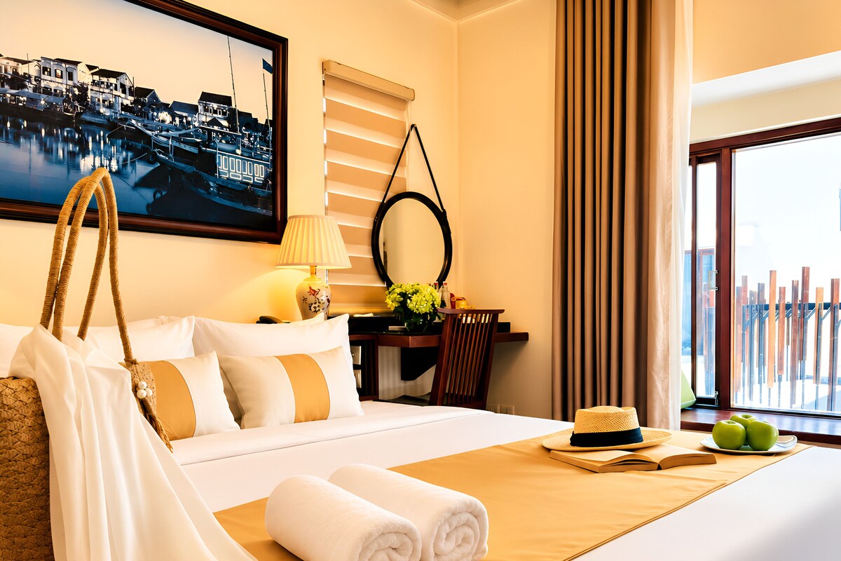 A hotel room with a bed, a desk, a chair, a lamp, a mirror, a window with curtains, and a view of a dock.