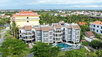 A multi-story hotel with a swimming pool, surrounded by greenery and other buildings.