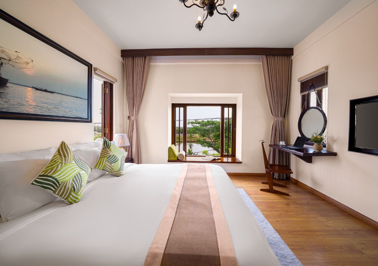 Habitación de hotel con una cama grande, vistas al exterior, un escritorio con una computadora portátil y un televisor.