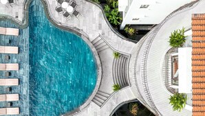 Una piscina en la azotea de diseño curvo, rodeada por una terraza de piedra y algunas sillas de descanso.