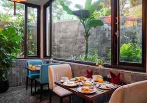 A dining area with a table set for two, surrounded by large windows with a view of greenery. - Faifo Boutique Hotel & Spa (Da Nang)