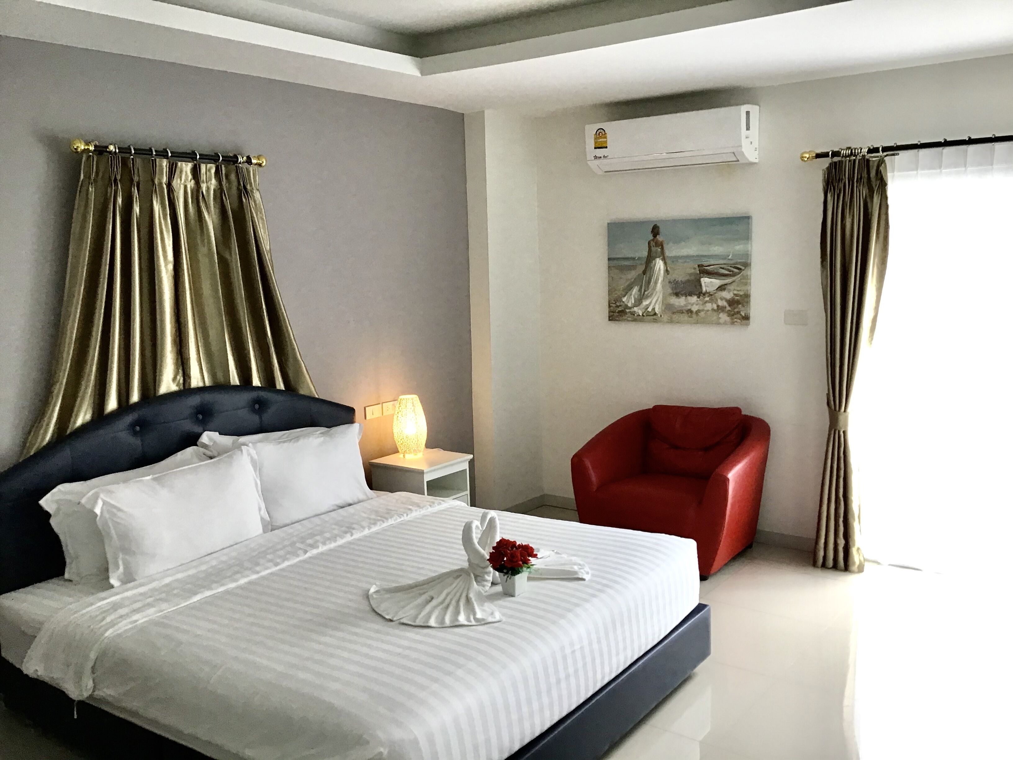 A hotel room with a large bed, a red armchair, a nightstand with a lamp, and a painting on the wall.