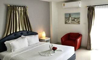 A hotel room with a large bed, a red armchair, a nightstand with a lamp, and a painting on the wall.