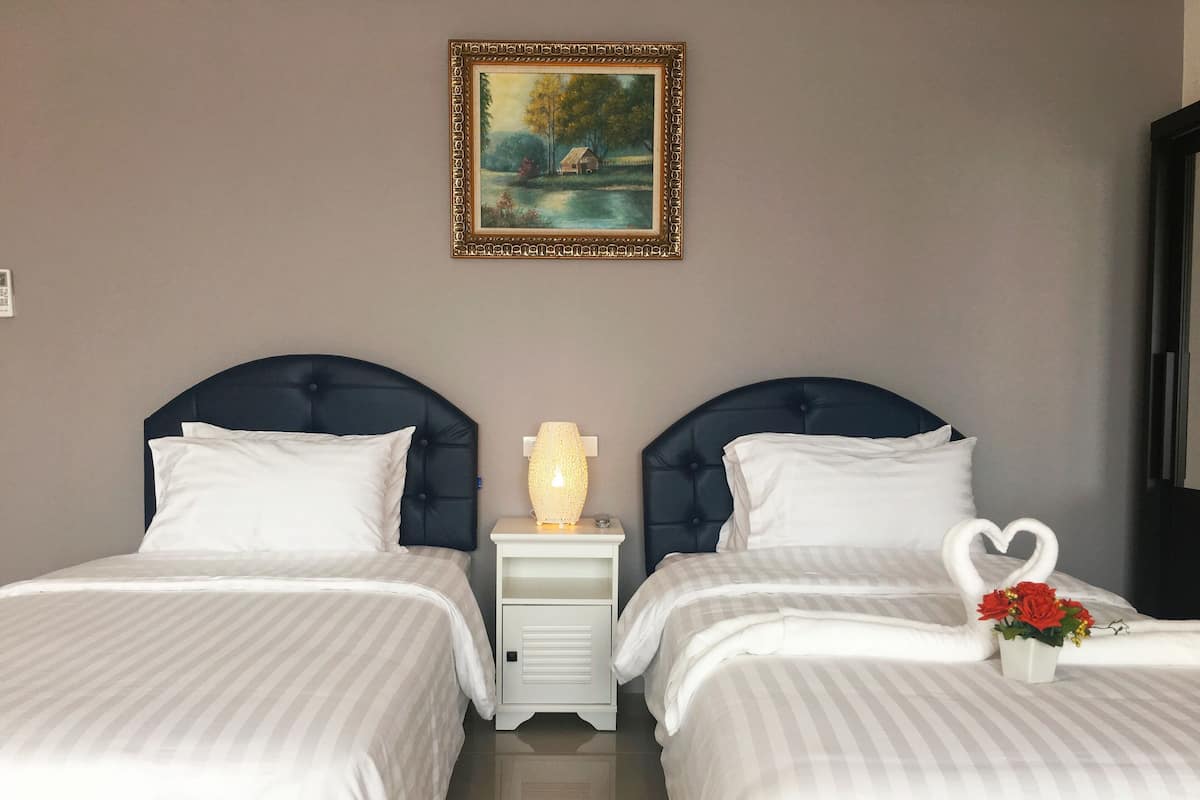 Une chambre d’hôtel avec deux lits, une table de chevet avec une lampe, un tableau au mur et un objet décoratif en forme de cœur sur le lit.