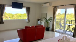 Une chambre d’hôtel avec un canapé rouge, un lit avec une literie blanche, une plante en pot et un balcon agrémenté de mobilier d’extérieur.