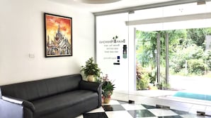 Un espace d’accueil avec un canapé en cuir noir, un sol à carreaux, un tableau encadré et une porte vitrée donnant sur l’extérieur.