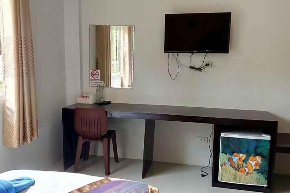 A hotel room with a bed, a desk, a chair, a television, and a small refrigerator.
