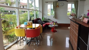 Una habitación luminosa con un ventanal grande, un mostrador de recepción de madera y una mesa roja y amarilla con sillas.