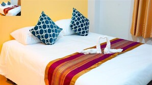 Una cama bien hecha con sábanas blancas, dos almohadas de estampado azul y una decoración de toallas en forma de cisne sobre una manta multicolora.