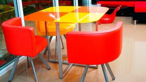 Un interior moderno con una mesa de vidrio rodeada por sillas rojas, un sofá rojo y vistas a la vegetación a través de grandes ventanales.