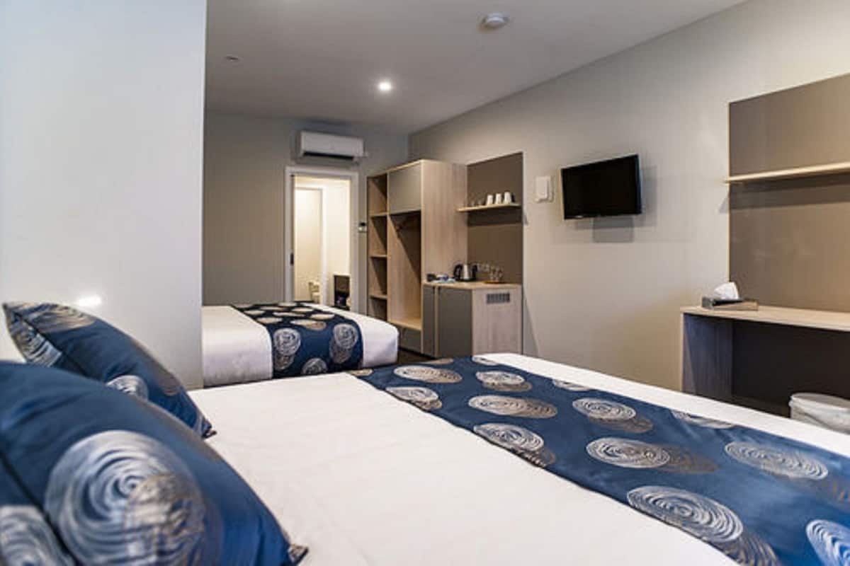 Habitación de hotel con dos camas, un televisor montado en la pared y una zona de kitchenette.