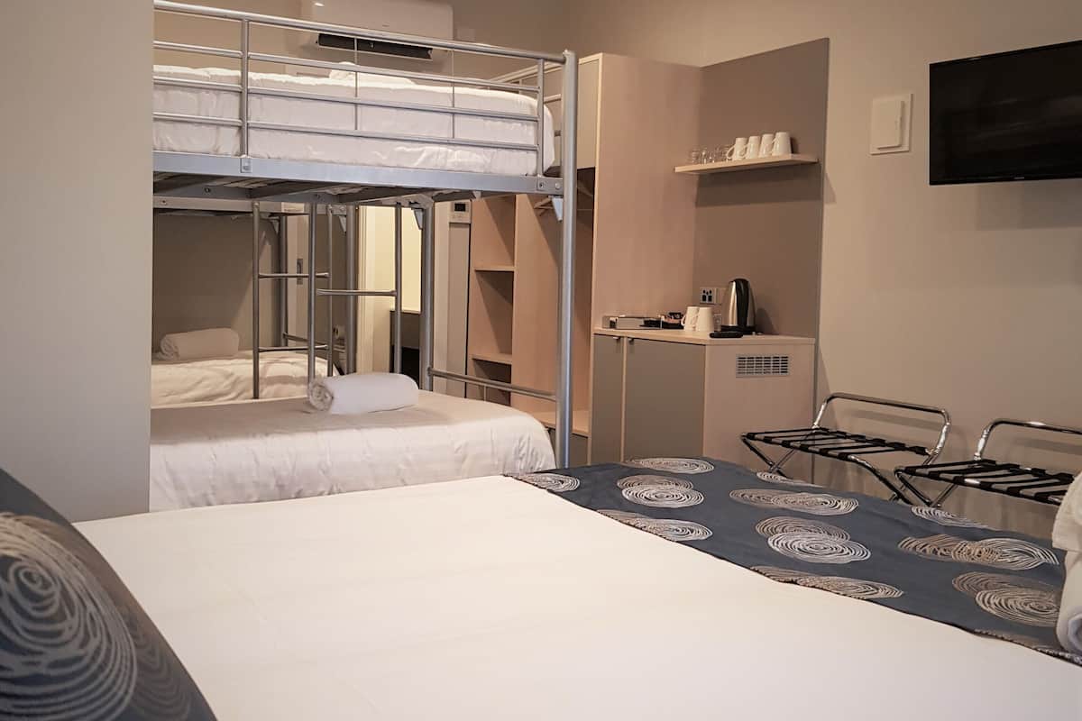 Una habitación de hotel con literas, un escritorio con hervidor, televisión y repisas con tazas.